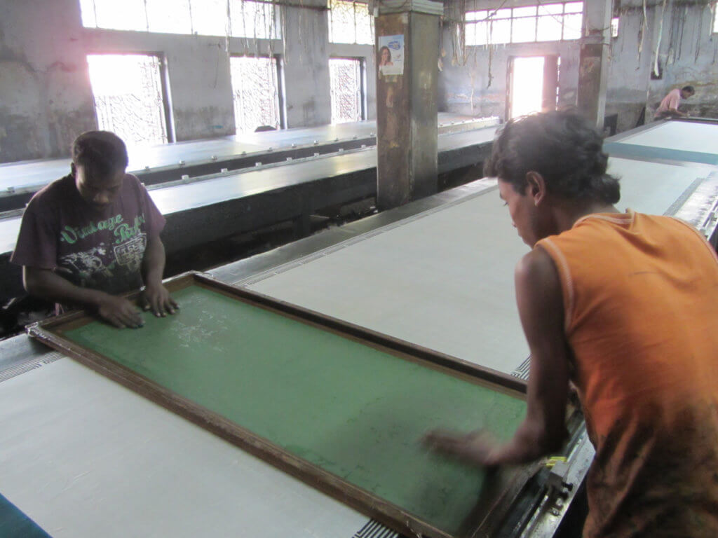 Workers at a Craft Resource Center-associated workshop in India prepare to paint silk using a patterned screen