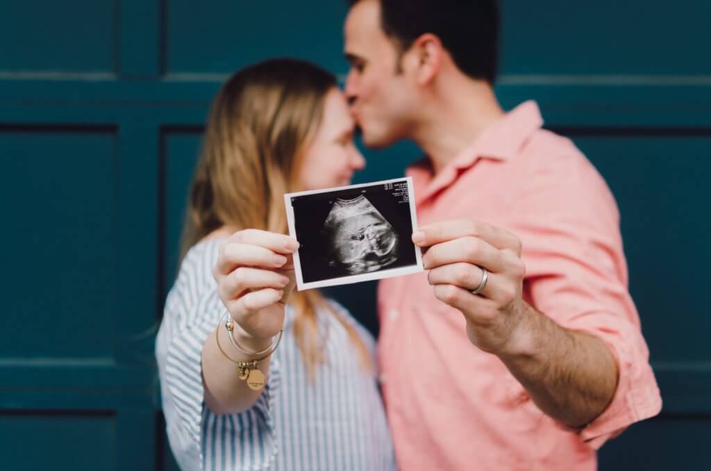 Parents kissing while holding an ultrasound of their baby