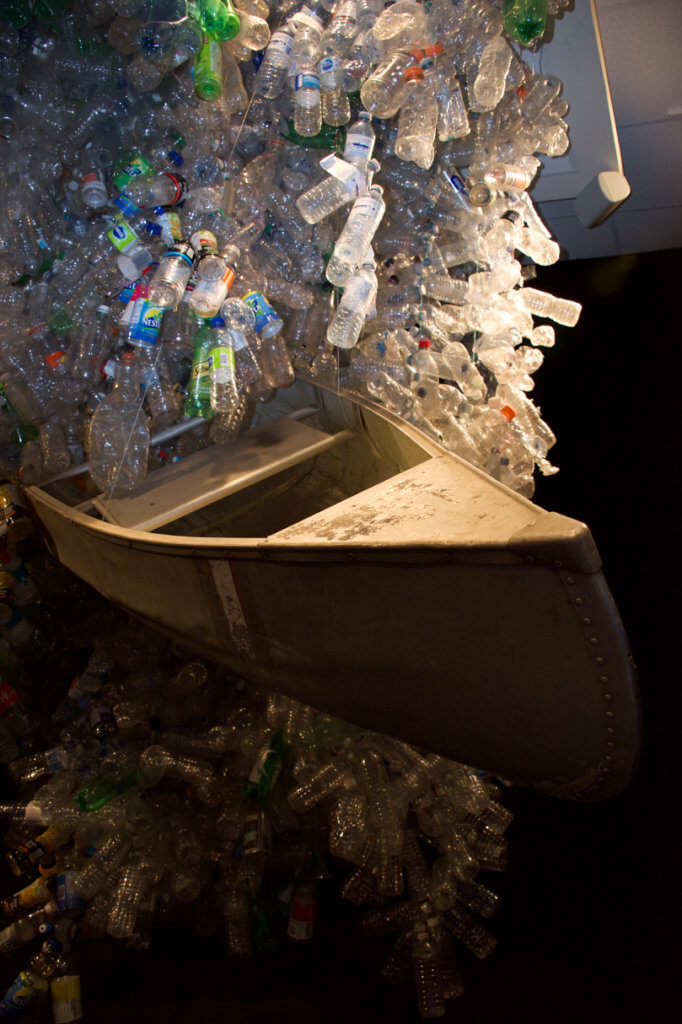 Over Our Heads, by Rebecca Jane Houston: a canoe lists, suspended in a cascade of plastic bottles